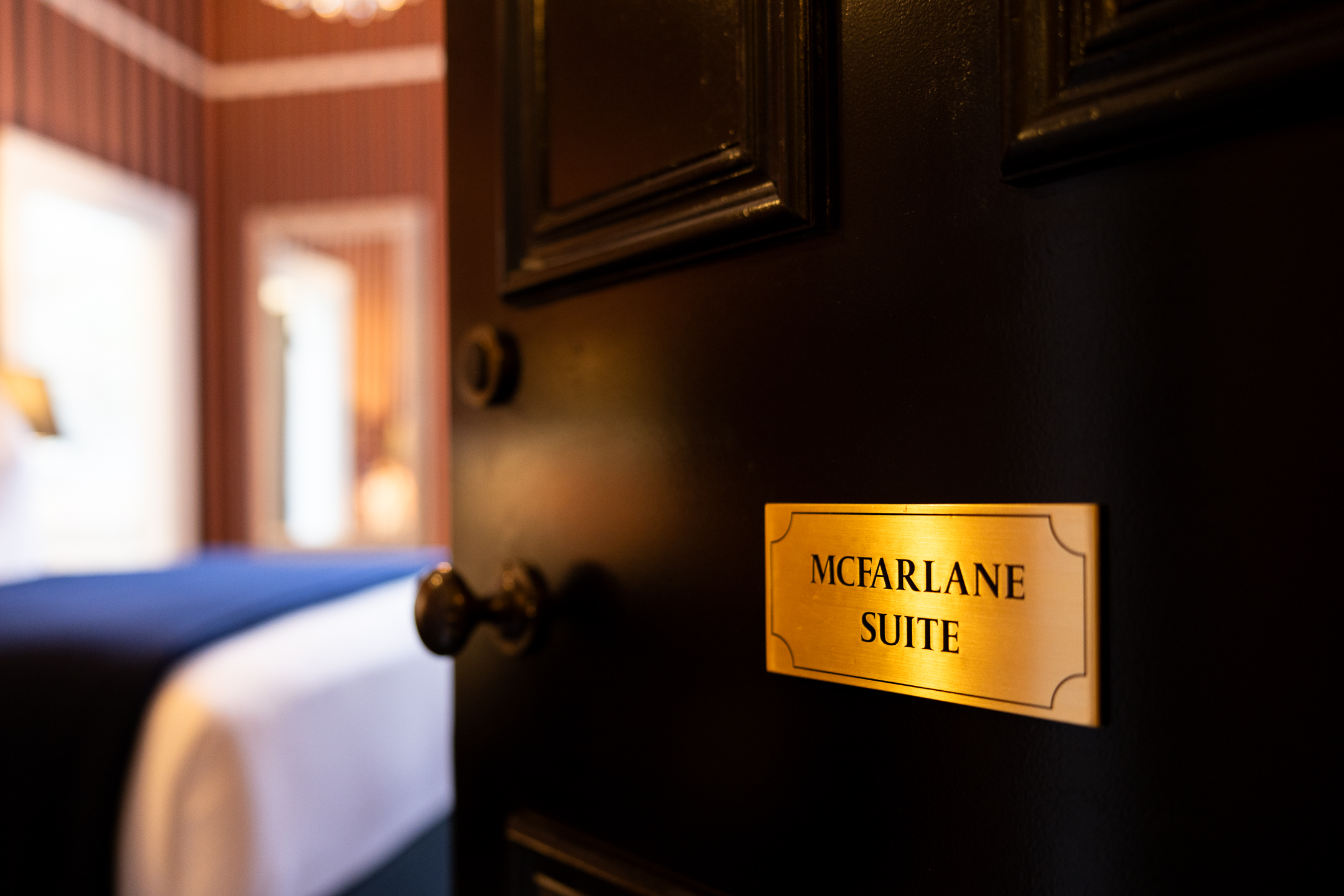 Entrance to the McFarlane Room at Hulbert House showing the brass plaque of the room name in the foreground and the bedroom in the background